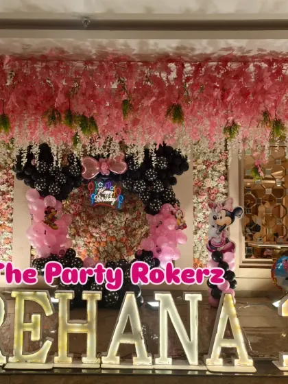 A stunning Minnie Mouse-themed first birthday. The main stage features large marquee letters, a floral backdrop, and a black and pink balloon arrangement.