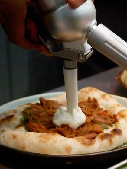 The espuma being added to the flatbread, covering the savory jackfruit meat with a cloud of potato and parmesan.