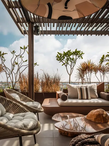 This angle highlights the layering of textures and greenery. Woven wicker chairs contrast with smooth stone tables, while tall grasses and frangipani trees frame the view, creating a lush, tropical minimalist garden retreat.
