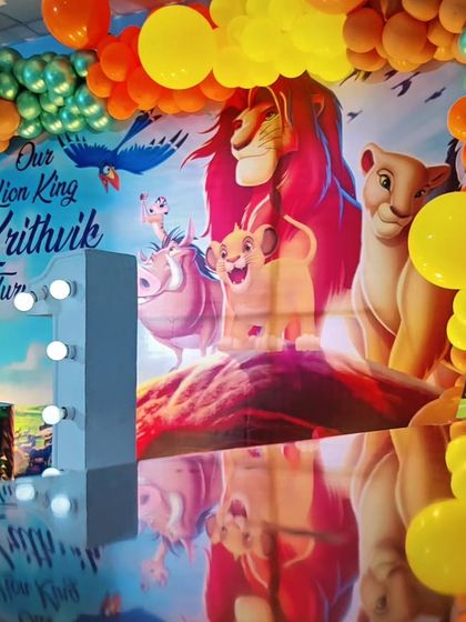 A majestic Lion King theme for a first birthday celebration. This setup features a large backdrop of Pride Rock, character-printed plinths, and a colorful balloon arch.