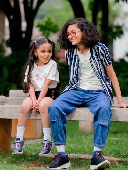 Another angle from a sibling photoshoot, capturing a sweet, interactive moment between the two sisters in a beautiful green space.