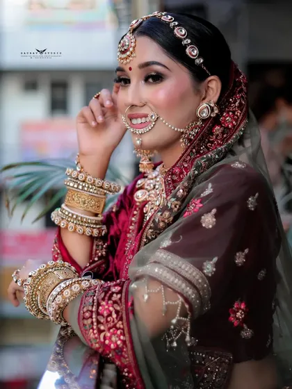 A candid, smiling portrait of the bride in a maroon lehenga, captured in natural outdoor lighting.