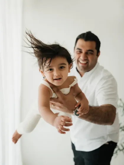 A father joyfully tosses his child in the air, creating a dynamic and fun action shot during their studio session.