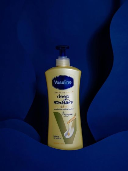 Minimal and classy. A clean, straight-on shot of the Vaseline deep moisture lotion against a custom-made wavy blue backdrop, emphasizing the product's shape and branding.