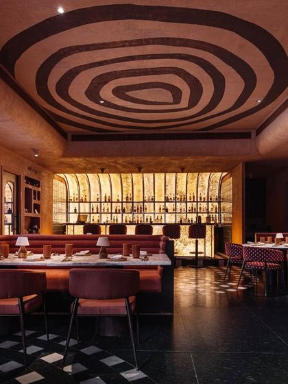 The ceiling at Idylll features a hand-painted, organic pattern that complements the earthy, monolithic feel of the space. The design of the bar and seating creates an intimate and immersive dining environment.
