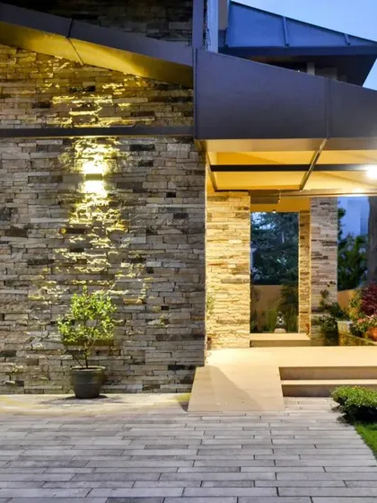 A close-up of the entrance pathway at dusk. Uplighting on the stacked stone wall adds drama and highlights the natural material, guiding visitors toward the front door.