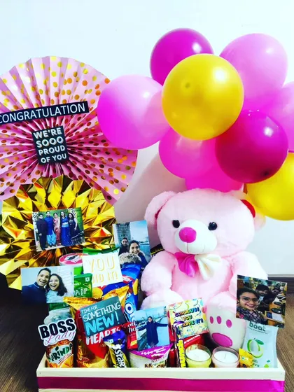 A bright and cheerful hamper to congratulate someone on a new job or promotion. It includes a large pink teddy bear, snacks, and fun 'Boss Lady' and 'You Did It' signs.