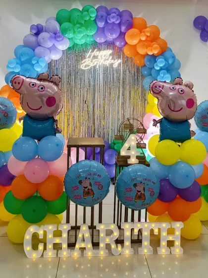 A colorful Peppa Pig themed 4th birthday. This setup includes a rainbow balloon arch, a silver tinsel backdrop, and foil balloons of George Pig.