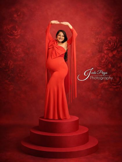 Posing on a tiered platform adds a sense of grandeur to this maternity portrait. The mom-to-be looks radiant in a one-shoulder red gown with dramatic fringed sleeves.