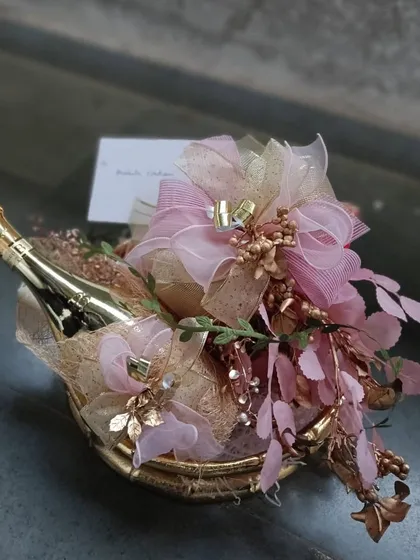 A toast to celebration. This compact and elegant hamper features a miniature champagne bottle adorned with pink and gold floral details, making it a perfect congratulatory gift or a luxurious party favor.