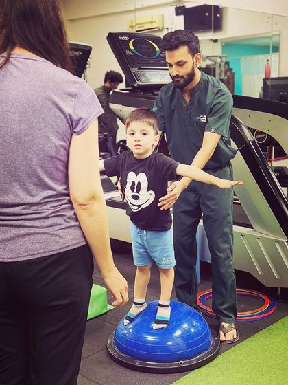 A young client in a Mickey Mouse shirt smiles while working on his balance with one of our therapists. We believe in making therapy a positive and empowering experience for children.