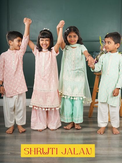 A happy group of siblings celebrating together in my coordinated pastel outfits. The girls are wearing sharara sets with pom-pom details, while the boys are in matching kurtas, all in soft pink and mint green.