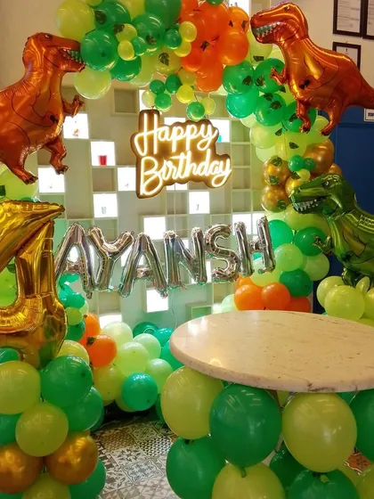A dinosaur-themed birthday is always a hit with the kids. This setup includes a custom balloon arch with T-Rex foil balloons, a neon "Happy Birthday" sign, and a matching balloon-wrapped table for the cake.