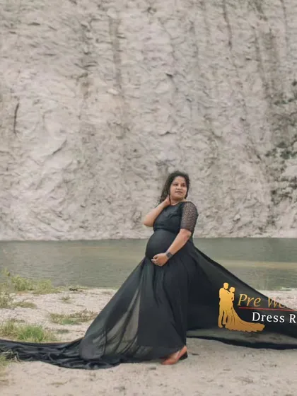 The black flying tail gown stands out against a rugged, natural cliffside. This image showcases how the gown's long train can be spread out to create a dramatic, grounded effect for your maternity photos.