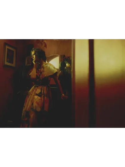 The heroine moves through a dimly lit hallway. The styling and the long, horizontal frame create a sense of passage and searching.