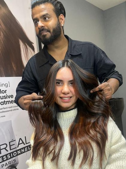 Another satisfied client with her stylist. Her hair features a beautiful blend of brown and lighter highlights, styled in soft, face-framing layers.