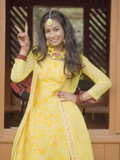 A fun and cheerful shot from a Haldi-themed or yellow-themed ethnic wear shoot. The model is making a peace sign, showing a playful personality.