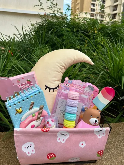 A sweet, dreamy hamper in pink with a moon-shaped pillow and other cute accessories. The key is to create a magical experience for the child.