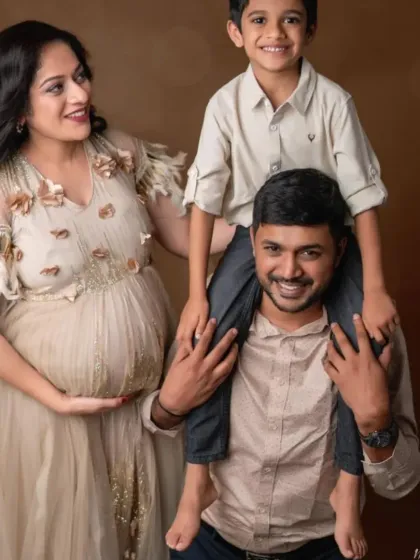 A joyful family portrait. The mom-to-be glows in our beige embellished gown while her son sits happily on his father's shoulders.