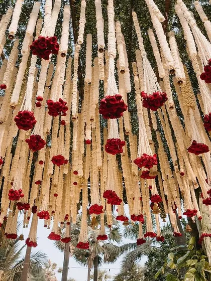 A view from below the mandap canopy, showing the dense arrangement of hanging tuberose and red rose clusters.