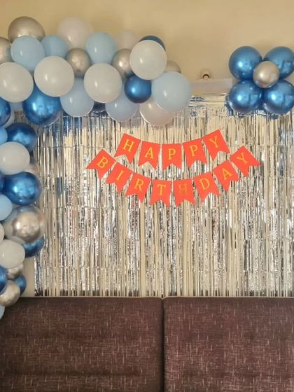 A simple and classic birthday decoration for a home, featuring a blue and silver balloon frame around a shimmer curtain.