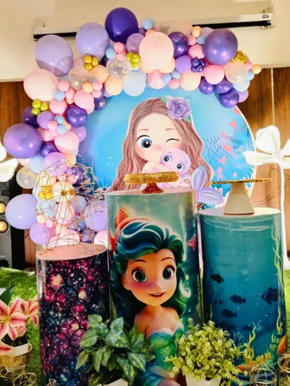 A close-up of the mermaid party setup, focusing on the character-themed pedestals and the balloon arch.