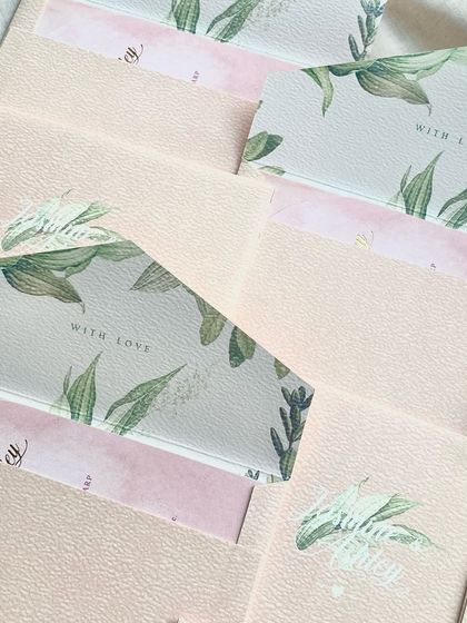 A collection of soft pink envelopes with a peek of the leafy green floral liners inside. The textured paper of the envelopes adds a tactile element to the suite.
