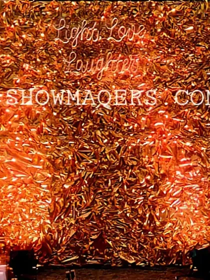 A glamorous photo wall with a shimmering gold foil backdrop and a 'Light, Love, Laughter' neon sign, surrounded by candles.