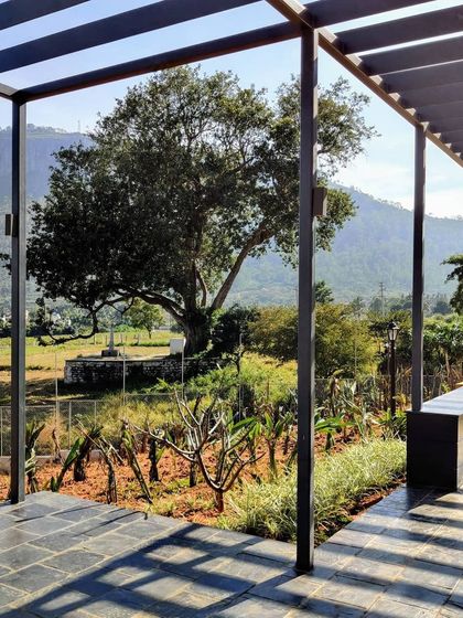 A shaded walkway with a pergola structure at the Nandi Hills home. This space provides a cool and comfortable path through the garden, with views of the surrounding landscape framed by the structure.