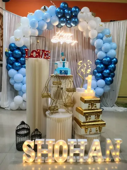 A delightful blue and white themed birthday setup, featuring a decorative golden ferris wheel prop for holding a cake or cupcakes.