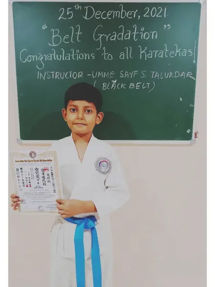 A happy karateka after the belt gradation ceremony. He proudly holds his certificate after earning his blue belt.