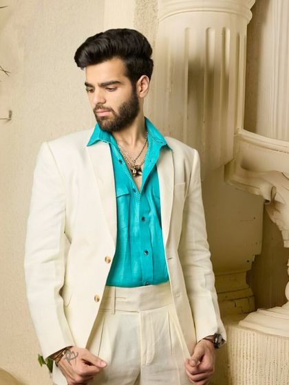 The off-white suit, paired with a bright turquoise shirt, creates a look that is both fun and refined, perfect for making a statement at any party or social gathering.