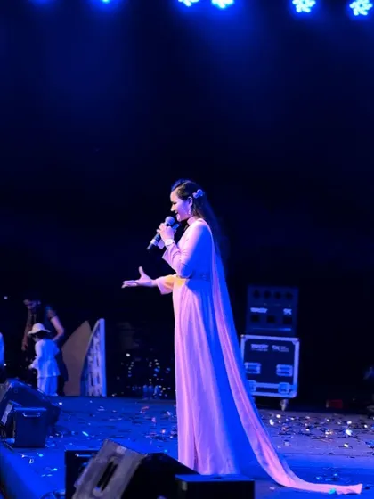 A side view of me hosting on stage under the cool blue lights of the Sangeet night.