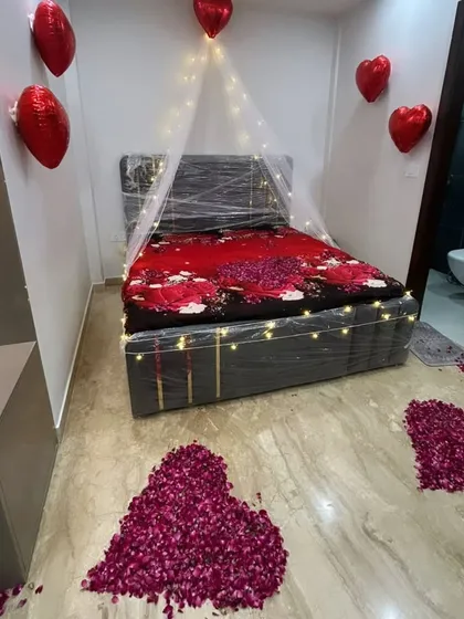 A simple yet beautiful romantic room setup. This decoration features a small fairy light canopy, heart-shaped foil balloons, and multiple hearts made from rose petals on the floor.