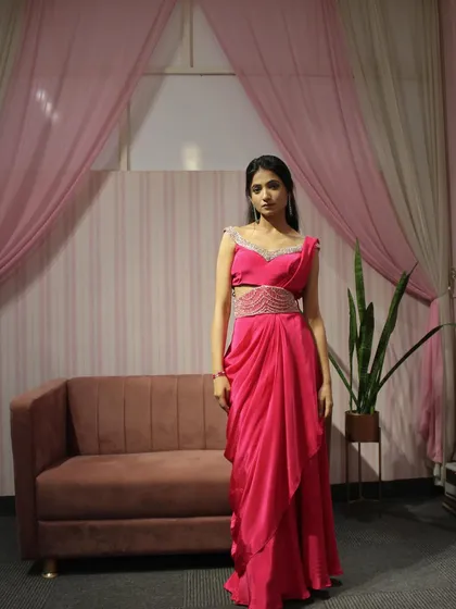 A full-length shot of our pink draped saree with a hand-embroidered belt. The off-shoulder blouse adds a modern touch.