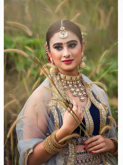 An outdoor bridal shoot capturing a serene and elegant moment. The natural setting complements the traditional lehenga, and the soft lighting highlights the delicate details of the fabric and embroidery.