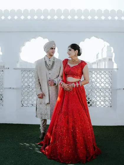 A regal couple portrait captured at a palace venue in Jaipur. The bride's vibrant red lehenga contrasts beautifully with the groom's elegant ivory sherwani, embodying the essence of a modern royal wedding.