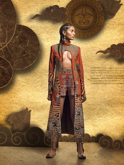 A conceptual fashion shoot featuring an intricately embroidered long jacket and shorts. The background, inspired by traditional art motifs, complements the garment's design, creating a cohesive and culturally rich visual narrative.