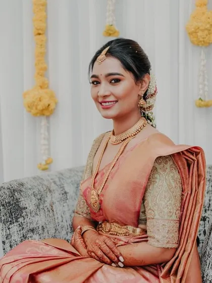 A full-length view of the bride in her peach saree, seated gracefully. The custom blouse and simple jewelry create a soft and romantic bridal look.