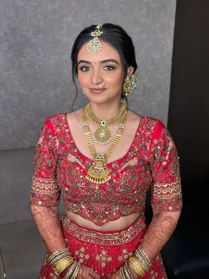 This soft bridal look in a traditional red lehenga is all about enhancing her natural features. The makeup is minimal but impactful, with a focus on radiant skin.
