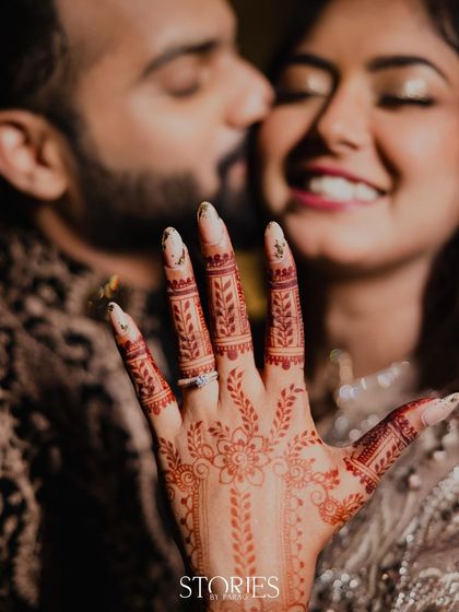 A perfect engagement shot focusing on the bride's intricately designed mehendi and the sparkling ring. In the background, the groom's gentle kiss on her cheek completes this story of love and commitment.