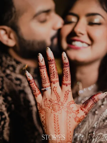 The moment after "yes". This beautiful shot focuses on her hand, adorned with intricate henna and the sparkling engagement ring, while the happy couple shares a kiss in the background.