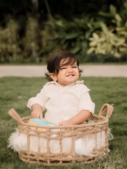 A happy little boy sitting in a basket, enjoying the fresh air during his outdoor milestone photoshoot.