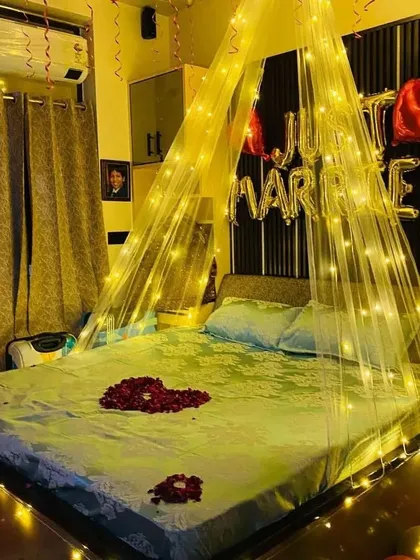 A view of the "Just Married" bed setup with a heart made of rose petals and a fairy light canopy creating a warm, inviting glow.