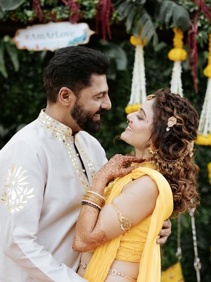 A sweet, intimate moment between the couple at their Haldi ceremony, surrounded by a backdrop of vibrant flowers and greenery.