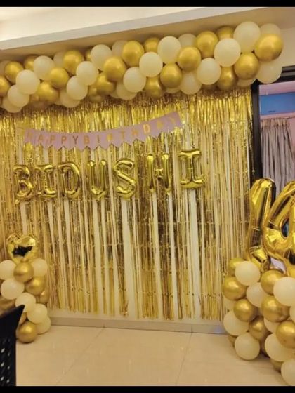 A 14th birthday celebration with a white and gold theme, featuring a foil curtain and personalized name balloons.