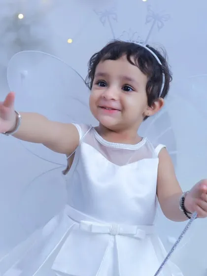 A happy little fairy reaching out with a welcoming smile. The all-white outfit and background create a pure and magical feel for this portrait.