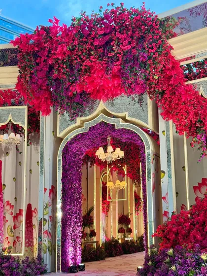A grand entrance to a vibrant celebration. The walkway is framed by an arch of red and purple flowers, leading guests into a world of color and magic.