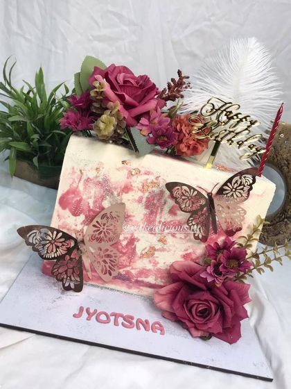 My first rectangular top-forward cake, and it came out so perfectly. This floral beauty features a white chocolate ganache with a pink textured effect, adorned with deep red roses, elegant butterflies, and a feather. The flavor inside is classic pineapple.