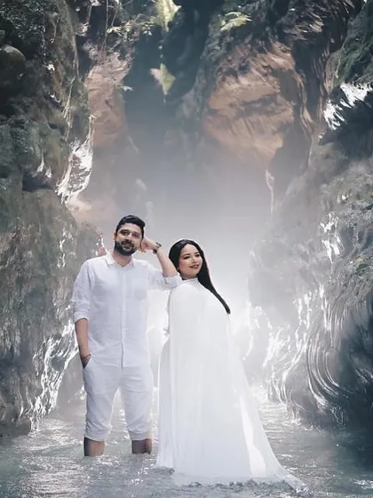 A powerful, wide-angle shot of the couple standing in the middle of a majestic cave, surrounded by rock formations.